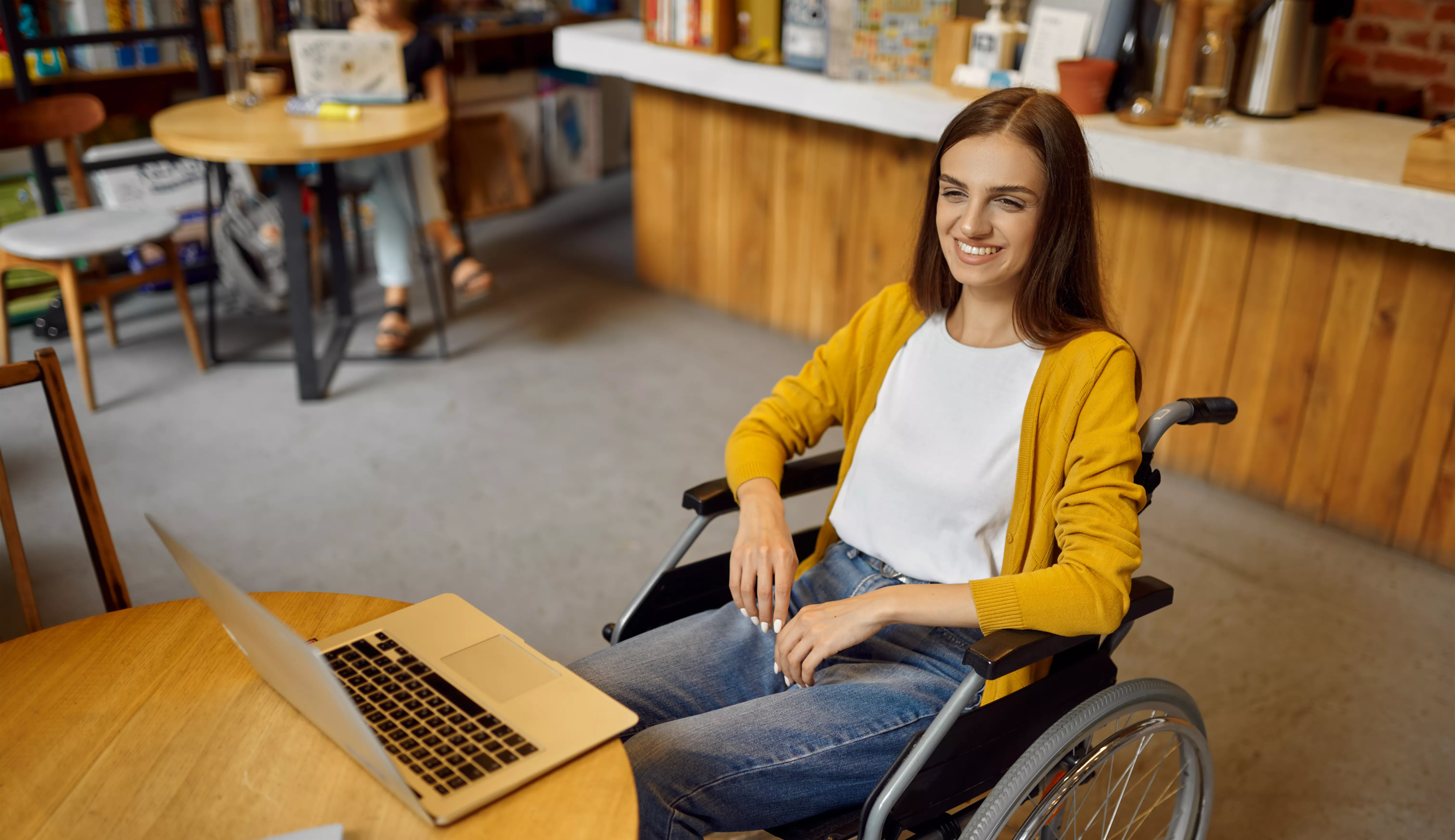 Image of a smiling female student in a wheelchair with a laptop open on a table