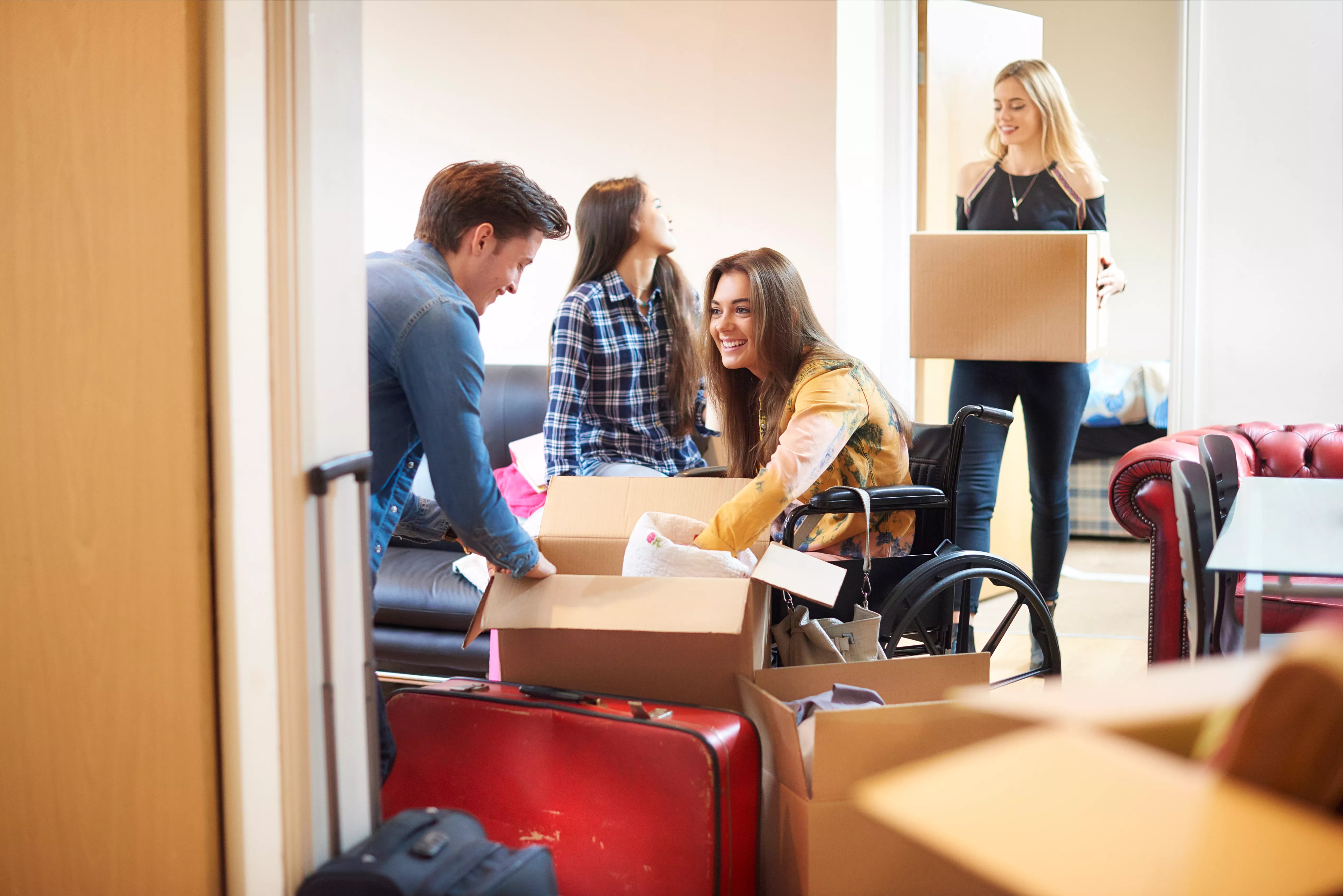 Image of students unpacking boxes as they move into student halls. One is a wheelchair user and she is in focus as she smiles at another student