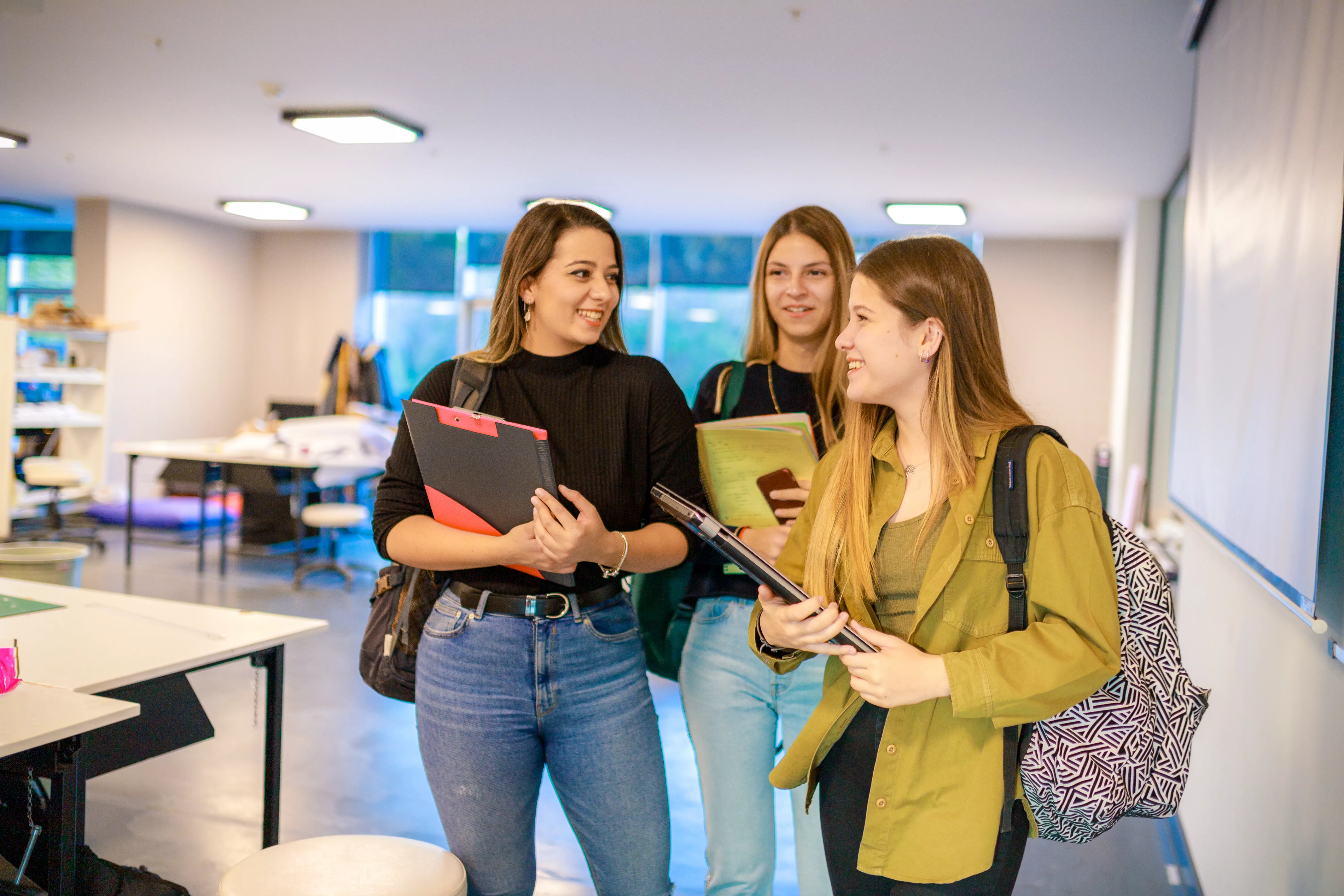 Image of three female students holding files and walking to a class