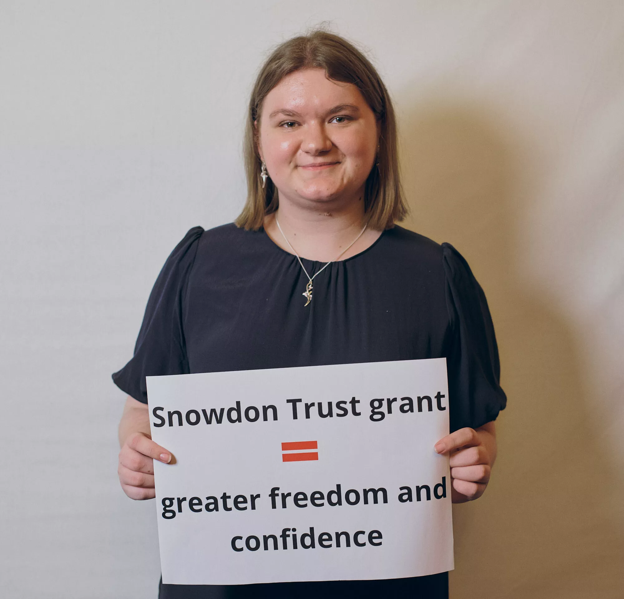 Image of a student smiling at the camera and holding a sign that says