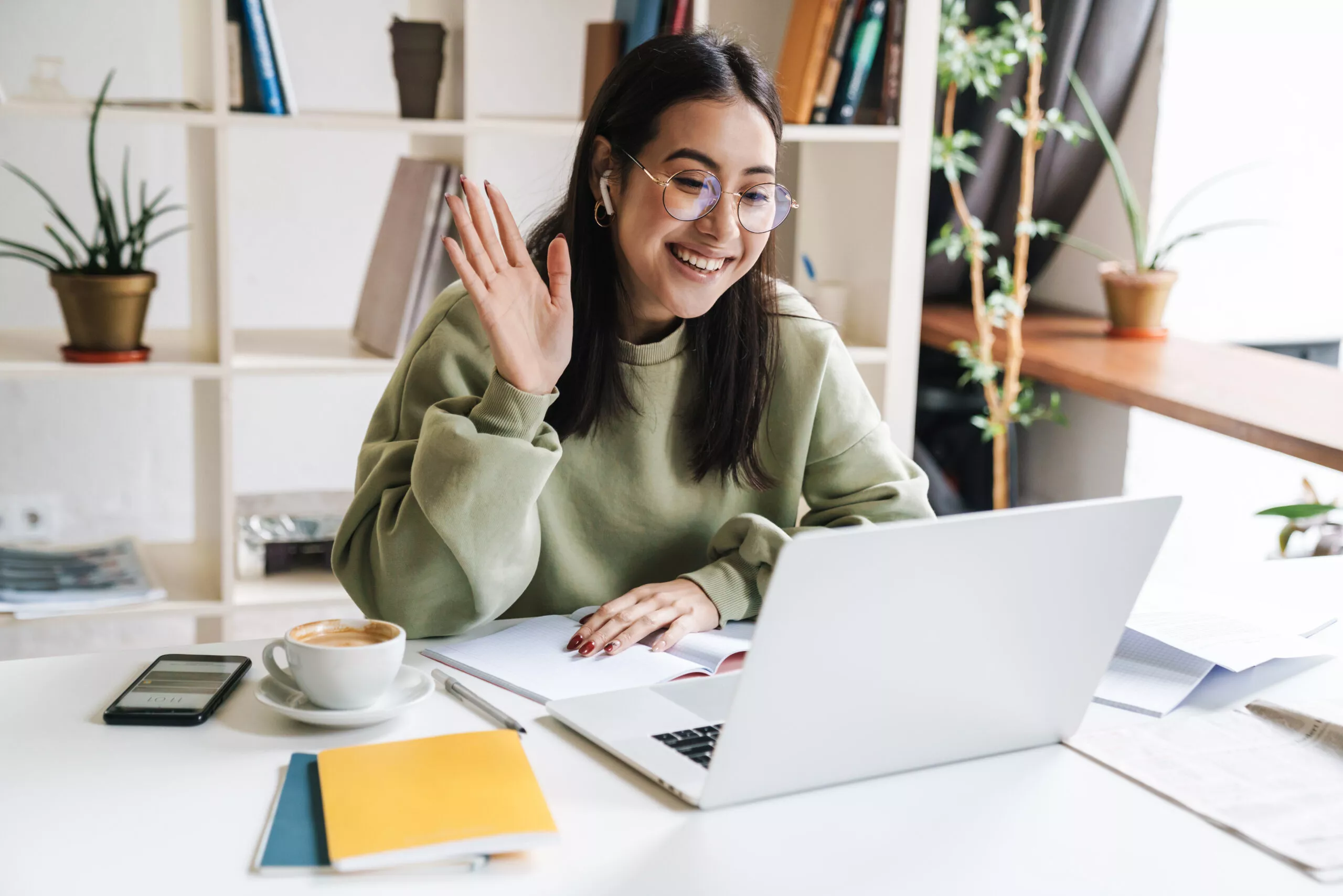 Image of a female student sitting at her laptop and waving during a video call