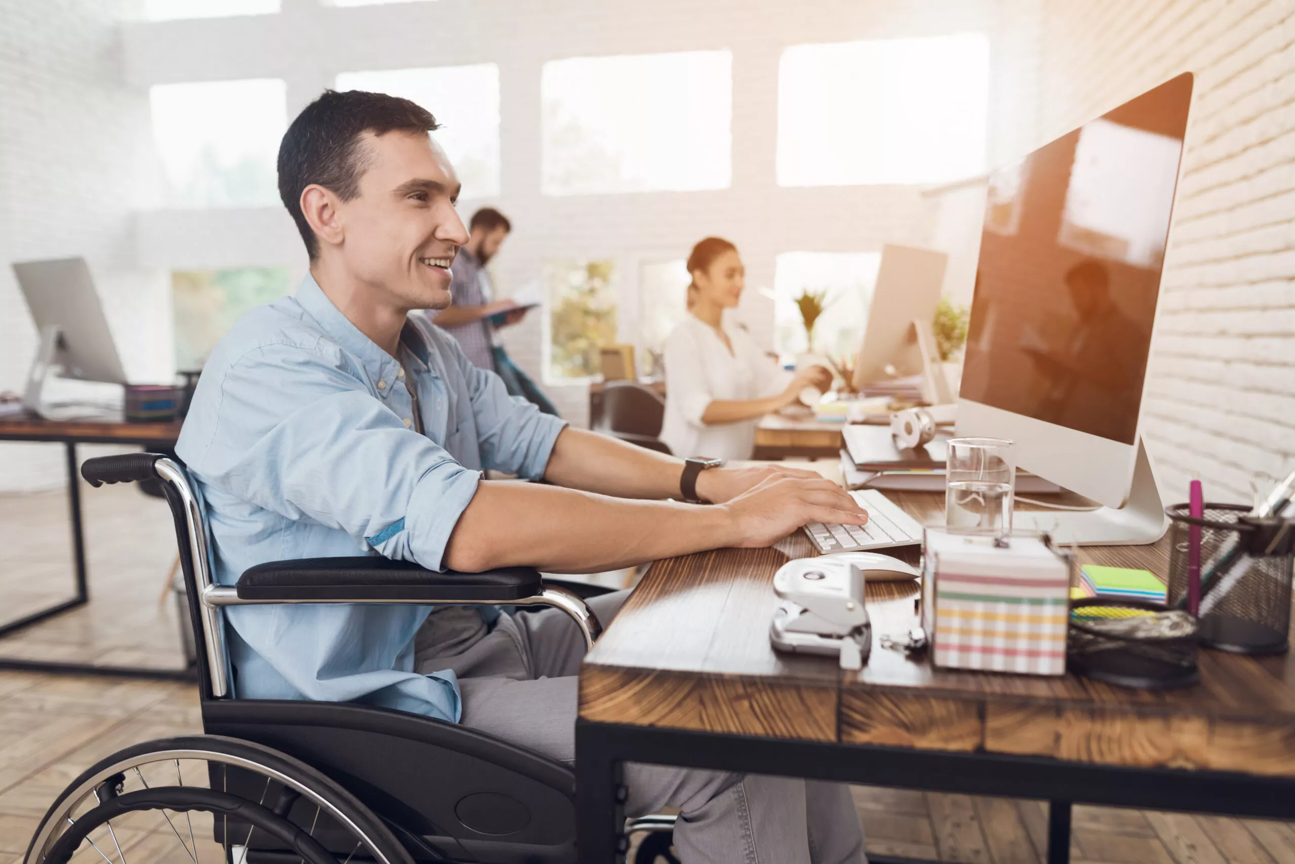 Image of a man sitting in a wheelchair working at a Mac in an office